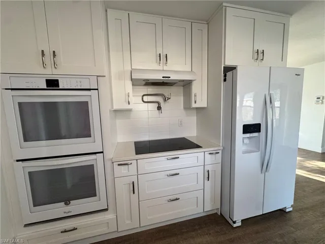 Kitchen with under cabinet range hood, white appliances, ceiling fan, light countertops, and dark wood-style flooring