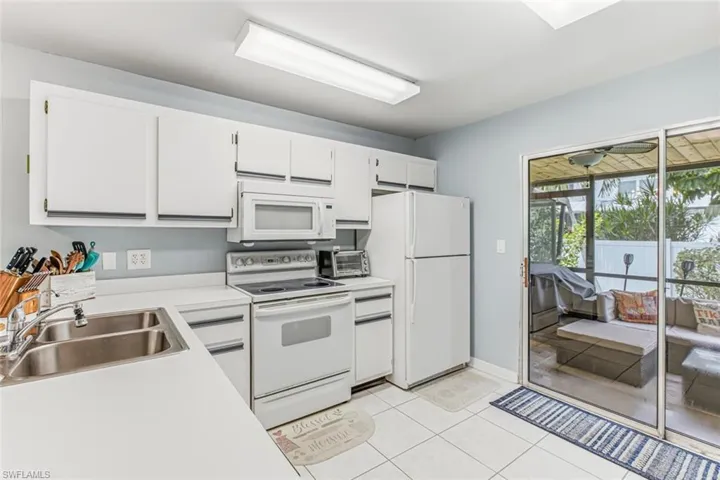 White cabinetry, light countertops, dual basin stainless steel sink, built-in microwave, and tile flooring