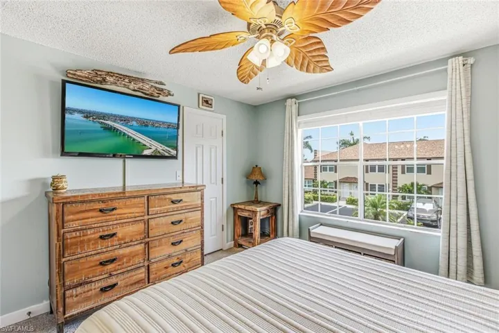 Window with white grid framing, wood-finish dresser with dark hardware, and a ceiling fan with leaf-shaped blades