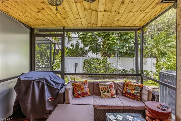 Screened outdoor living space with a wood-plank ceiling, black frame enclosure, and privacy landscaping