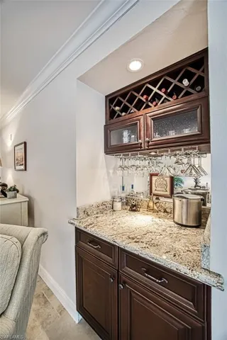 Bar featuring crown molding, light stone countertops, and dark brown cabinetry