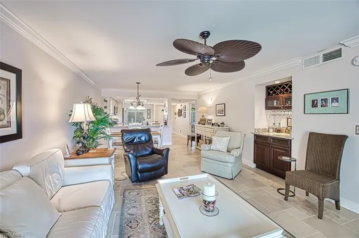 Living room featuring crown molding, ceiling fan with notable chandelier, and bar area