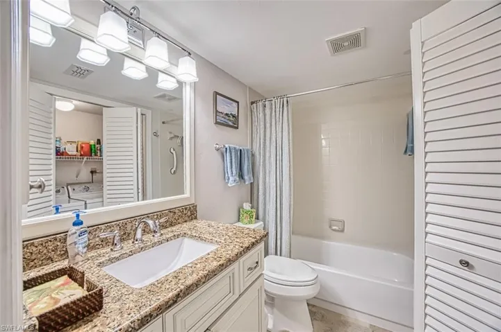 Full bathroom with vanity, independent washer and dryer, toilet, and shower / bath combo with shower curtain