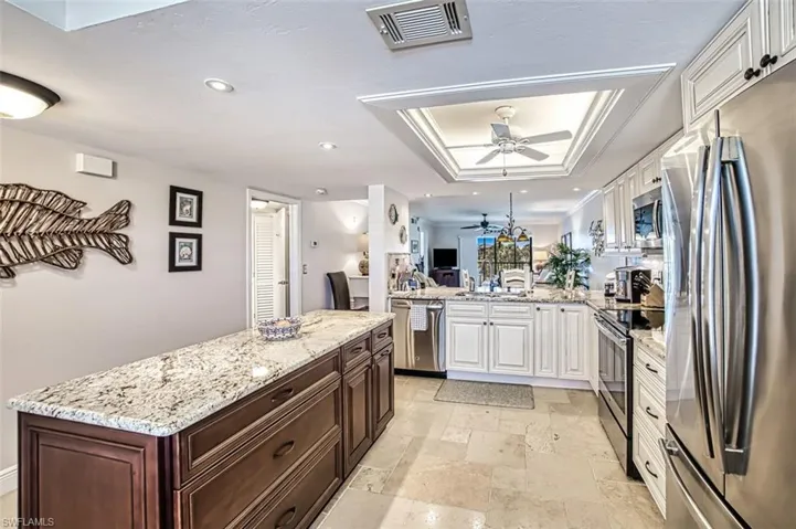 Kitchen featuring stainless steel appliances, a raised ceiling, white cabinetry, and kitchen peninsula