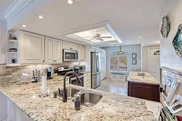 Kitchen featuring appliances with stainless steel finishes, tasteful backsplash, sink, a raised ceiling, and crown molding