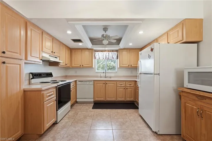 Kitchen with white appliances, light brown cabinetry, light countertops, light tile patterned floors, and recessed lighting