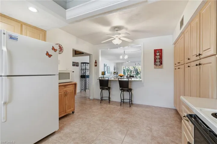 Kitchen with white appliances, a breakfast bar area, light brown cabinetry, light tile patterned floors, and ceiling fan