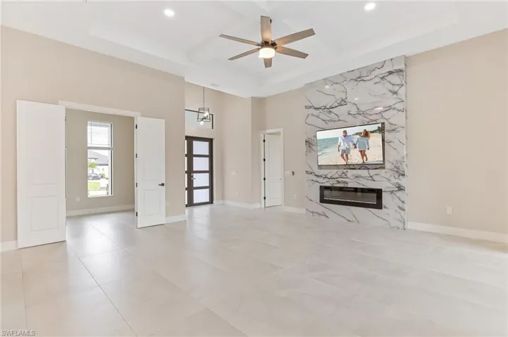 Unfurnished living room with coffered ceiling, beam ceiling, a fireplace, ceiling fan, and a high ceiling