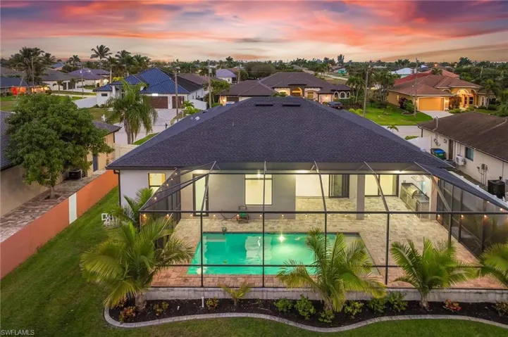 Back of property at dusk with a lanai, a shingled roof, an outdoor pool, a fenced backyard, and a residential view