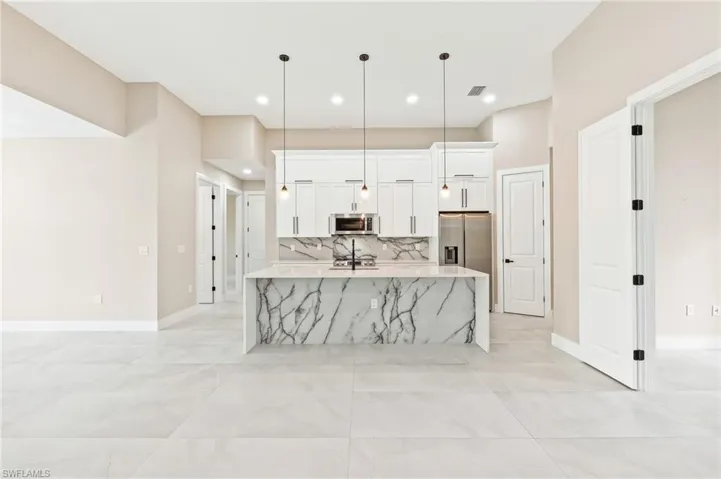 Kitchen with light stone countertops, white cabinets, hanging light fixtures, decorative backsplash, and stainless steel appliances