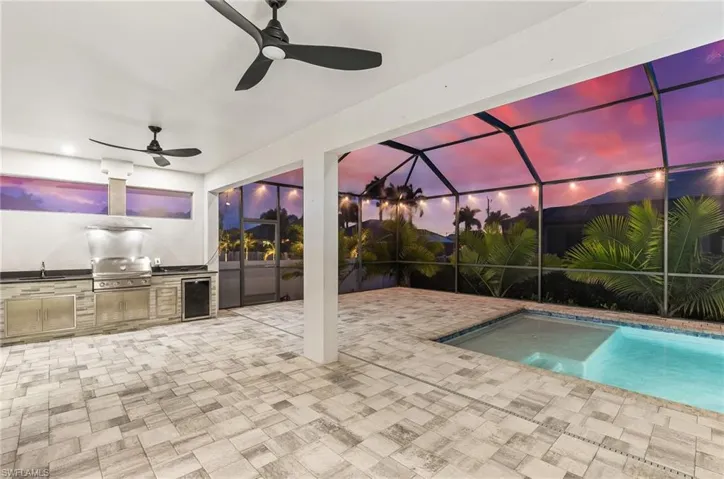 Pool at dusk featuring glass enclosure, exterior kitchen, a sunroom, an outdoor pool, and a patio