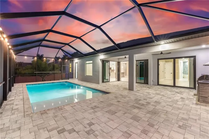 Pool at dusk featuring a sunroom, a lanai, and a patio