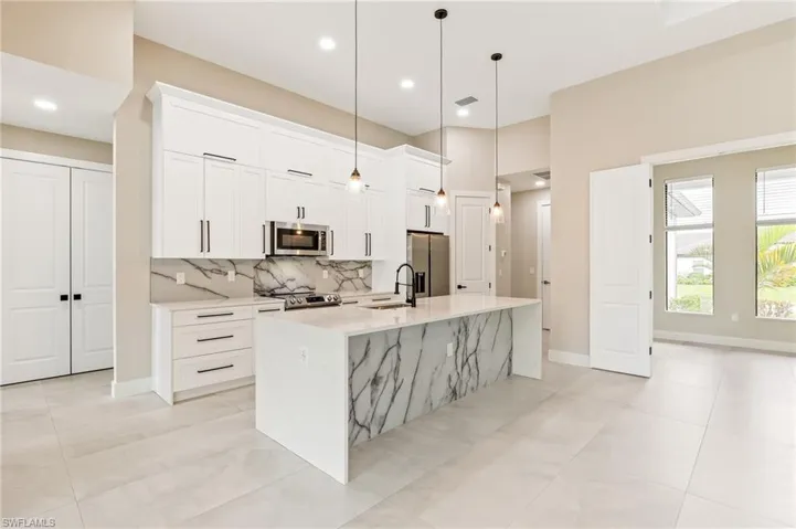 Kitchen with appliances with stainless steel finishes, hanging light fixtures, white cabinetry, light stone counters, and tasteful backsplash