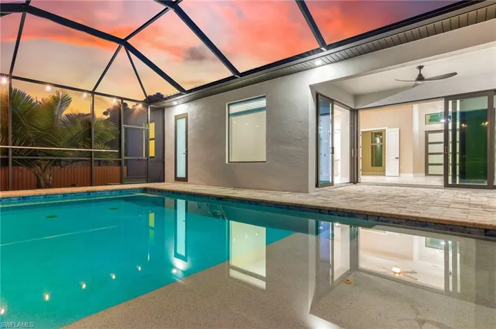 Pool at dusk with an outdoor pool, a sunroom, a patio, and a lanai