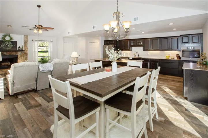 Dining room featuring a stone fireplace, wood-type flooring, and high vaulted ceiling