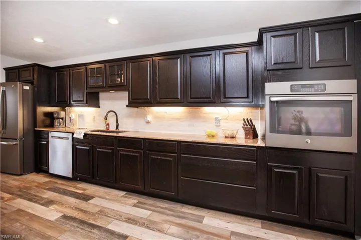 Kitchen with tasteful backsplash, sink, dark brown cabinetry, stainless steel appliances, and light hardwood / wood-style flooring
