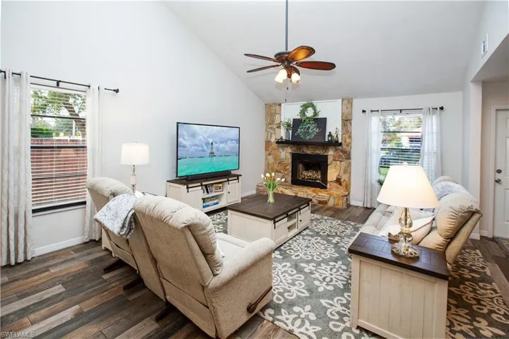 Living room featuring ceiling fan, high vaulted ceiling, a fireplace, and dark hardwood / wood-style flooring