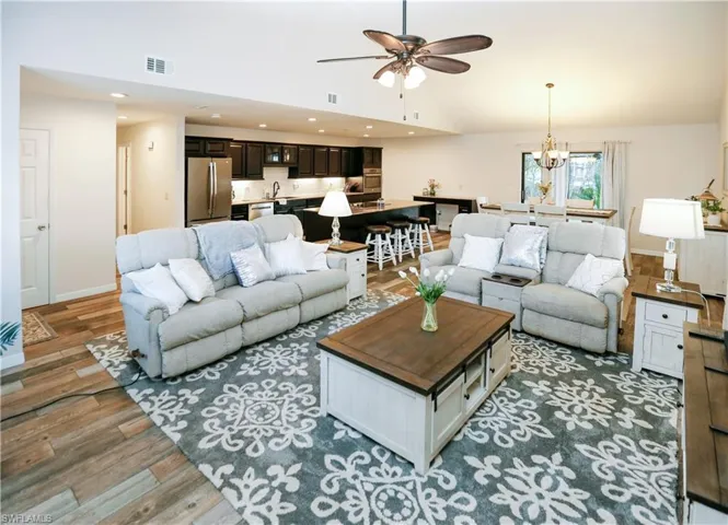 Living room with ceiling fan with notable chandelier, wood-type flooring, sink, and high vaulted ceiling