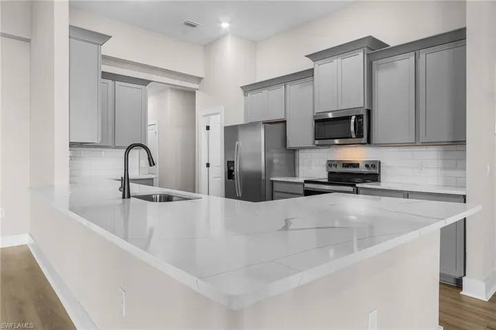 Kitchen featuring gray cabinetry, light wood finished floors, a peninsula, and decorative backsplash