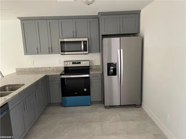 Kitchen with stainless steel appliances, light stone counters, and gray cabinetry