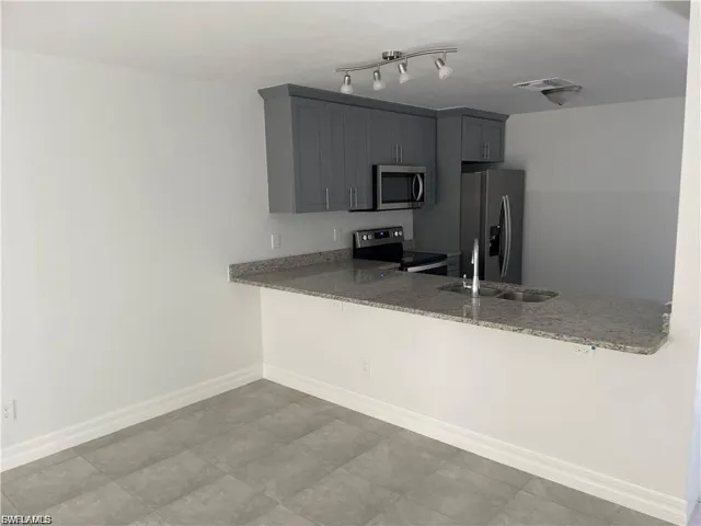 Kitchen with light stone counters, stainless steel appliances, gray cabinets, and a peninsula