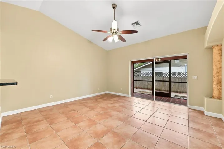 Vaulted ceilings enhance this room featuring tile flooring, a ceiling fan, and sliding glass doors leading to a screened patio