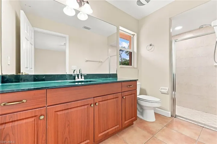 Spa-inspired primary bathroom showcasing warm wood cabinetry with ample storage, a striking turquoise countertop, dual sink configuration, and a spacious walk-in shower with tile surround and frameless glass enclosure
