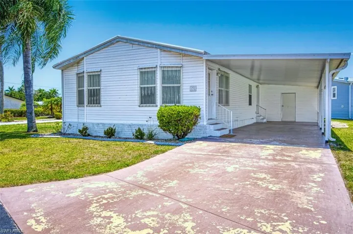 Manufactured / mobile home featuring entry steps, a front lawn, concrete driveway, and a carport