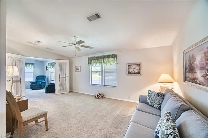 Living area with vaulted ceiling, light colored carpet, a textured ceiling, a ceiling fan, and baseboards