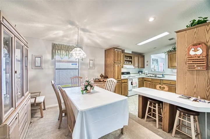 Dining room featuring a chandelier, light carpet, vaulted ceiling, baseboards, and a textured ceiling