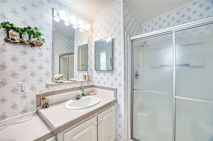 Bathroom with wallpapered walls, a textured ceiling, ornamental molding, a shower stall, and vanity