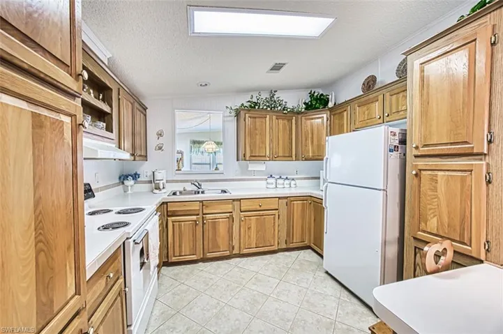 Kitchen featuring white appliances, a sink, a textured ceiling, light tile patterned floors, and light countertops