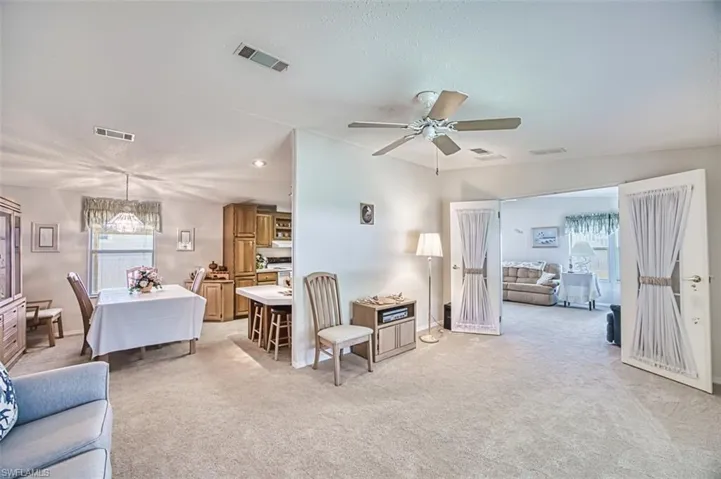 Living area featuring healthy amount of natural light, light colored carpet, a ceiling fan, and a chandelier