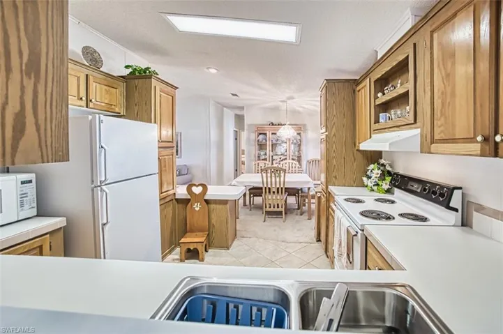 Kitchen featuring white appliances, brown cabinetry, light countertops, and a textured ceiling