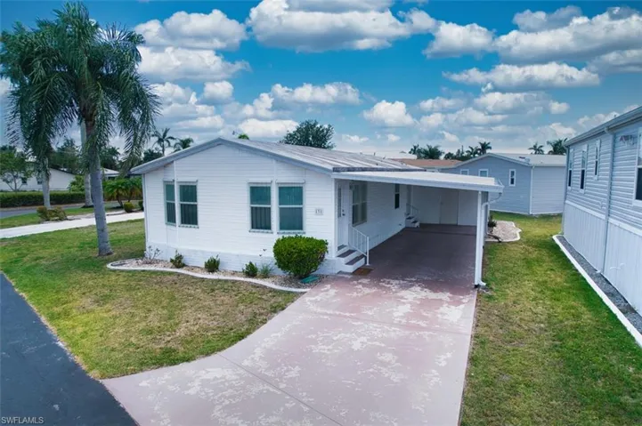 Manufactured / mobile home featuring driveway, a front lawn, an attached carport, and entry steps