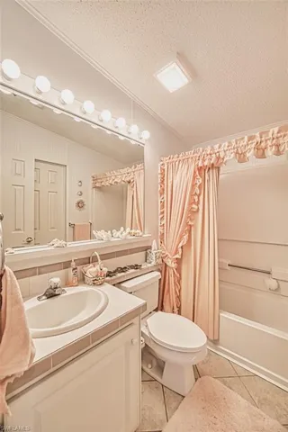 Bathroom featuring a textured ceiling, vanity, tile patterned floors, toilet, and ornamental molding