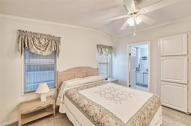 Bedroom with ornamental molding, light colored carpet, vaulted ceiling, ensuite bathroom, and a ceiling fan