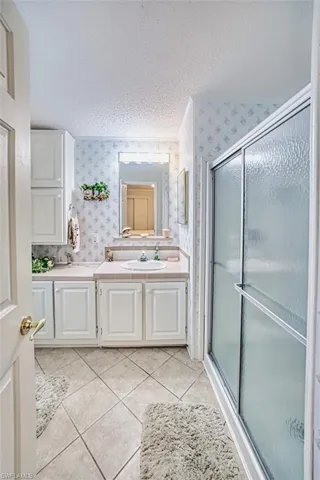 Full bath featuring wallpapered walls, vanity, a shower stall, tile patterned floors, and a textured ceiling