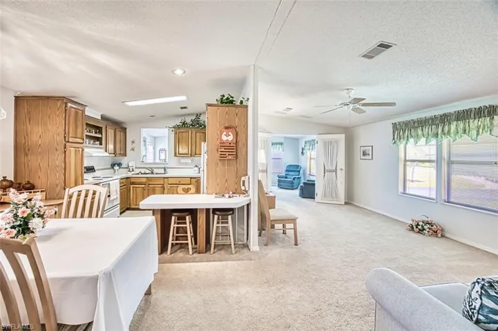 Kitchen with white electric stove, open floor plan, a textured ceiling, light countertops, and light carpet