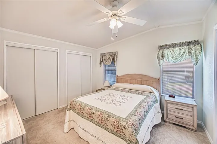 Bedroom with light carpet, two closets, crown molding, vaulted ceiling, and a ceiling fan