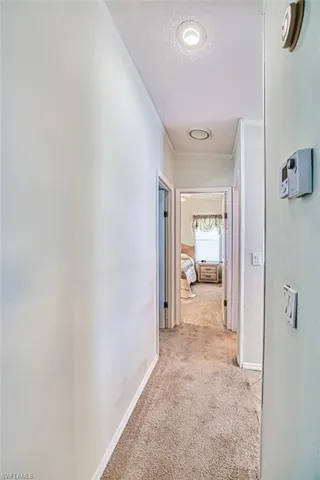 Hallway with crown molding, light carpet, a textured ceiling, and baseboards