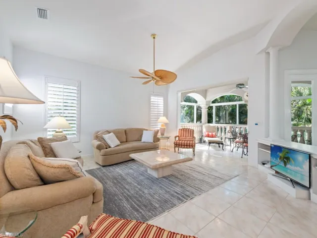 Living area with vaulted ceiling, decorative columns, light tile patterned flooring, and a ceiling fan