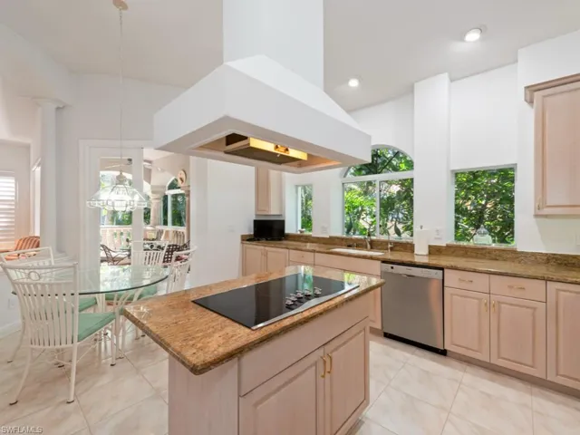 Kitchen featuring decorative light fixtures, light stone counters, a center island, stainless steel dishwasher, and island range hood