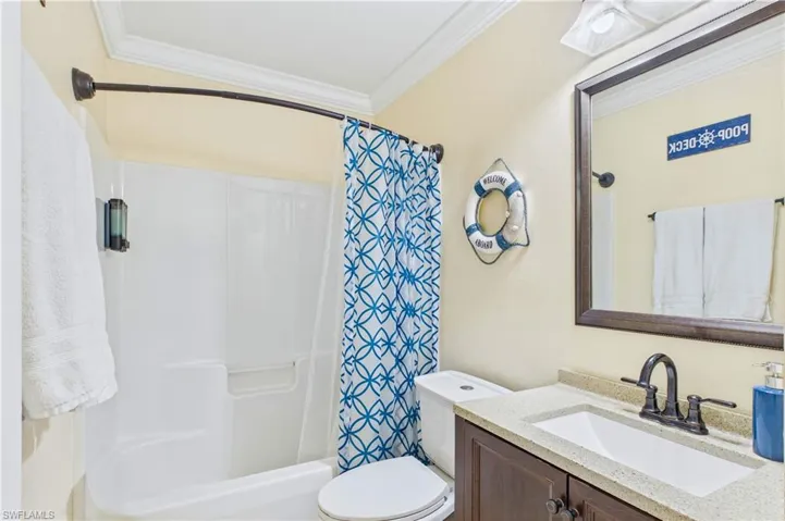 Bathroom featuring a white tub/shower combination with a curved shower rod, a dark wood-finish vanity with a light-colored countertop, and an integrated sink with a dark bronze-finish faucet