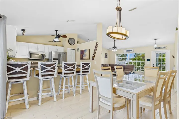Open-concept living space featuring a dining area with a glass-top table, a kitchen island with seating for four, white cabinetry, and stainless steel appliances