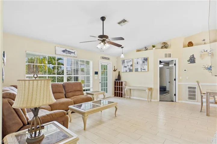 Spacious living area featuring light-toned tile flooring, vaulted ceilings, and a ceiling fan with light fixture