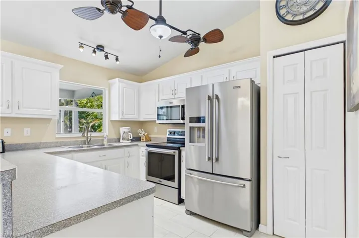Bright kitchen featuring white cabinetry, light-toned countertops, stainless steel appliances, a double basin sink, and tile flooring