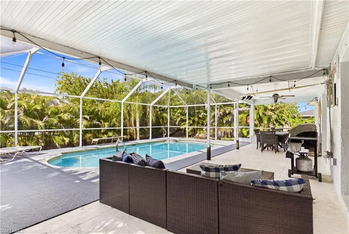 Screened pool enclosure featuring a curvilinear pool, ample patio space, a covered lanai, a ceiling fan, and string lighting