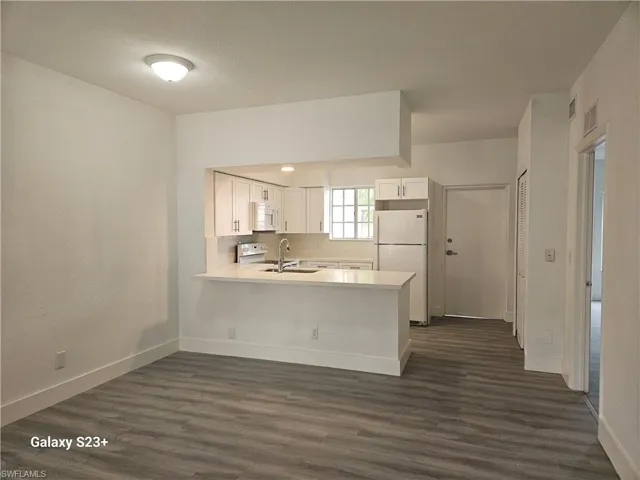 Kitchen with sink, white cabinetry, dark hardwood / wood-style floors, kitchen peninsula, and white appliances