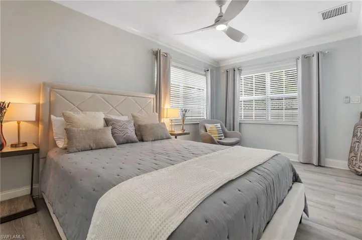 Bedroom with wood finished floors, ornamental molding, multiple windows, and ceiling fan